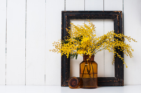 Home decor, mimosa yellow spring flowers in a vintage bottle on the white wall backgroundの写真素材