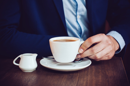 Businessman in a blue jacket with a cup of coffee in the cafe at the table, close-upの写真素材
