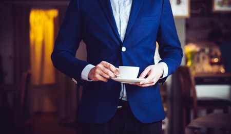 Businessman in a blue jacket standing with a cup of coffee in the cafe, close-upの写真素材