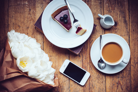 Bouquet of tulips, coffee with milk, cheesecake and smartphone on a shabby wooden floor, hipster...
