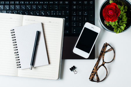 Office tabletop, home office: a laptop, notebooks, reading glasses, smart phone, pen on a white backgroundの写真素材
