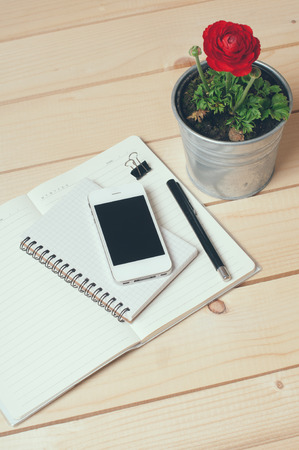 Rustic tabletop, home office: notebooks, smart phone, pen and a flowerの写真素材