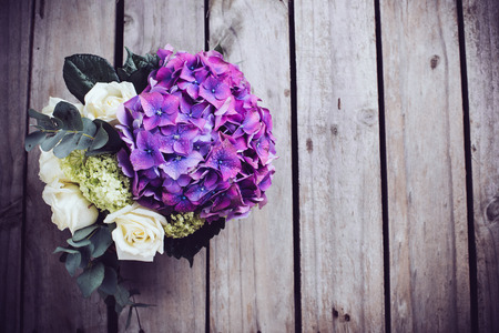 Big bouquet of fresh flowers, purple hydrangeas and white roses in a wicker basket on an old wooden board, vintage styleの写真素材