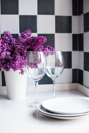 Spring bouquet of lilacs in a vase and glasses on the kitchen table by the wall, home interiorの写真素材
