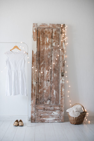 Summer dress, vintage wooden door, basket and decorative lights, girls room interior decoration with white walls and floors.の写真素材