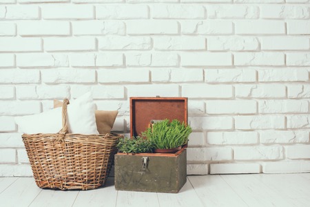 Wicker basket with a pillow and green home plant at the white brick wall on the floor, rustic home interior decorの写真素材