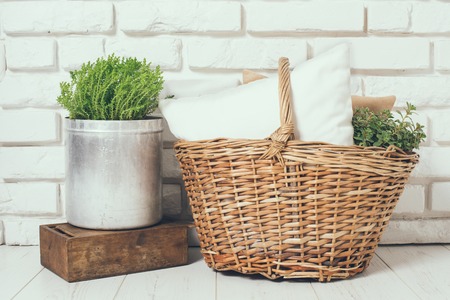 Wicker basket with a pillow and green home plant at the white brick wall on the floor, rustic home interior decorの写真素材