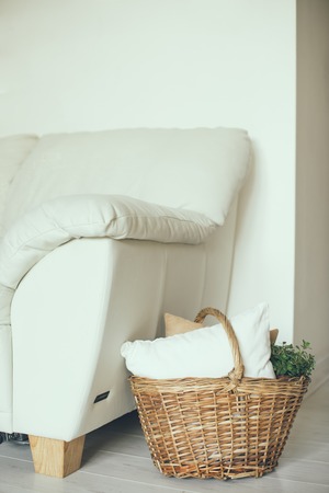 Wicker basket with pillows and green home plant on a floor by the sofa, modern home interior decorの写真素材