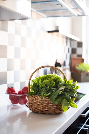 Wicker basket with fresh greens, basil, arugula and spinach on the table in the interior of a modern home kitchen.の写真素材