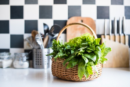 Wicker basket with fresh greens, basil, arugula and spinach on the table in the interior of a modern home kitchen.の写真素材