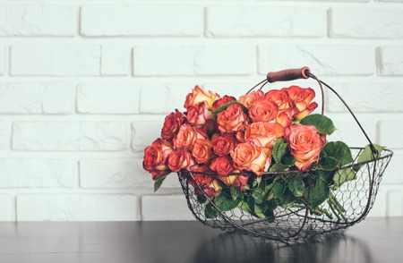 A bouquet of roses in a basket on a shelf near the white brick wallの写真素材