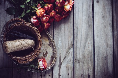 Floristic background, a bouquet of roses, scissors and twine in a basket on an old vintage wooden board.の写真素材
