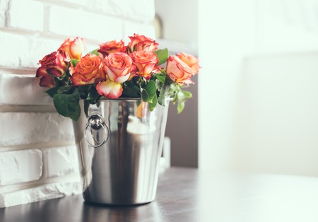 Bunch of fresh roses in a metal bucket for champagne on a table in a bright interior roomの写真素材