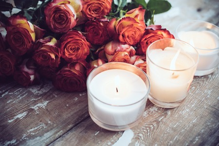 Vintage holiday decor, a bouquet of red roses and burning candles on an old wooden board surface, wedding decorationの写真素材