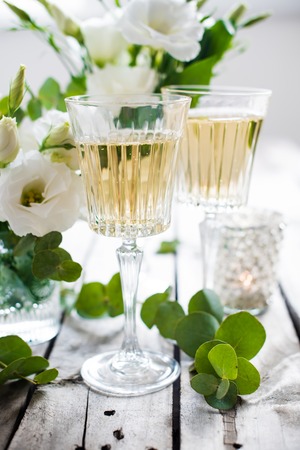 Two glasses of champagne and white flowers, candles on an old vintage rustic wooden table. Vintage summer wedding table decoration. Festive decor.の写真素材