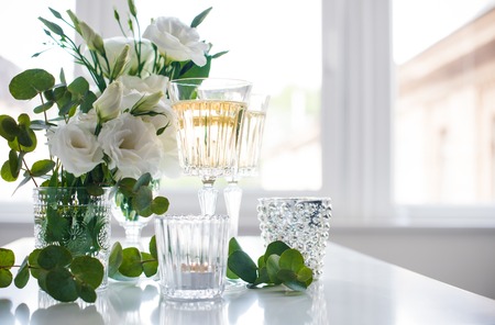 Two glasses of champagne and white flowers, candles on white table.の写真素材