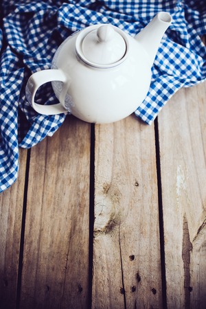 Large white porcelain teapot and a blue linen napkin on old wooden board, rustic kitchen background.の写真素材