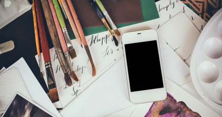 Smartphone on the table in the artist's studio, watercolor paints, brushes and sketches, palette and painting tools. Arts and modern technology, hipster style.の写真素材