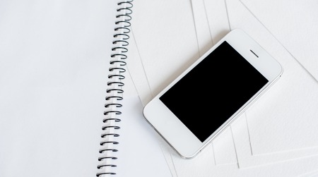 Smartphone and clean empty white paper sheets on office table with copy space, business and communicationの写真素材