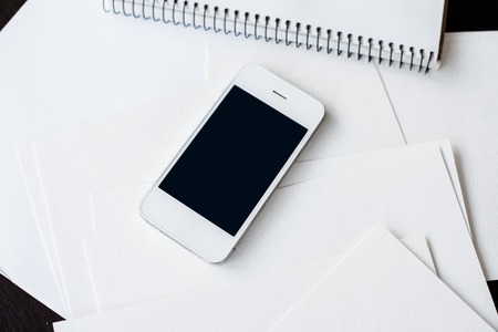 Smartphone and clean empty white paper sheets on office table with copy space, business and...