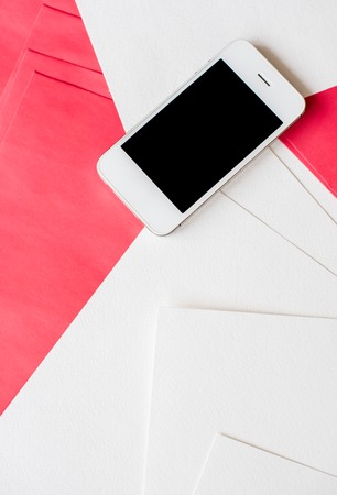 Smartphone and clean empty white and red paper sheets on office table with copy space, business and communication backgroundの写真素材