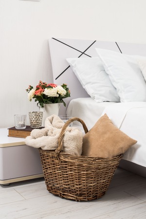 Interior of white bedroom, new linens on the bed, cozy home. Wicker basket and pillows closeup.の写真素材