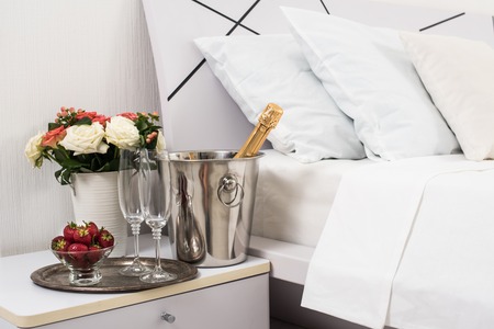 Champagne in bed in a hotel room, ice bucket, glasses and fruits on white linenの写真素材