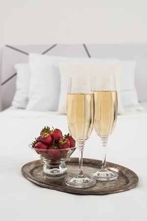 Champagne in bed in a hotel room, ice bucket, glasses and fruits on white linenの写真素材