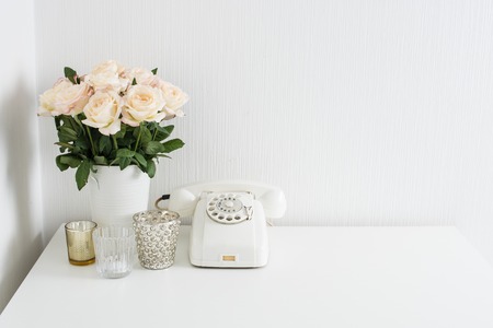 Modern interior decor with vintage details: white rotary phone and fresh flowers on a table. Clean white room in real apartment.の写真素材