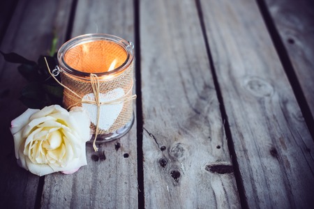 Burning candle in a decorative jar and flower of rose on old wooden board. Rustic decor.の写真素材