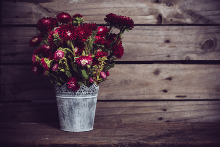 Rustic red flowers in a can vase on an old vintage wooden board backgroundの写真素材