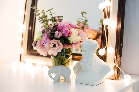 Vintage mirror, flowers and warm lights on a chest. Retro interior decoration.の写真素材