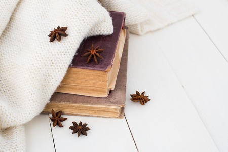 Winter still-life, old vintage books and knitted sweater on white painted wooden background.の写真素材
