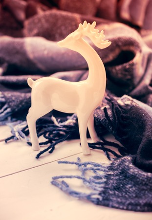 Beautiful white ceramic Christmas deer and a blue checkered woolen plaid. Cozy winter holiday home arrangement.の写真素材