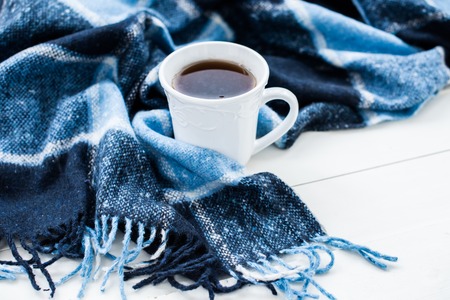 Beautiful white cup of hot tea and a blue checkered woolen plaid. Cozy winter home arrangement.の写真素材