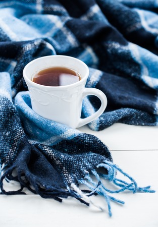 Beautiful white cup of hot tea and a blue checkered woolen plaid. Cozy winter home arrangement.の写真素材