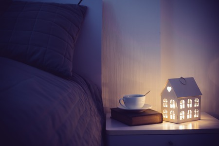 Cozy evening bedroom interior, cup of tea and a night light on the bedside table. Home interior decor with warm light.