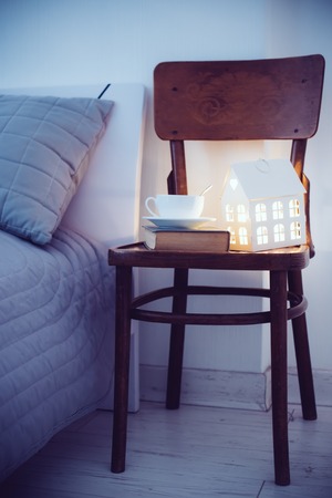 Cozy evening bedroom interior, cup of tea and a night light on the bedside table. Home interior decor with warm light.の写真素材