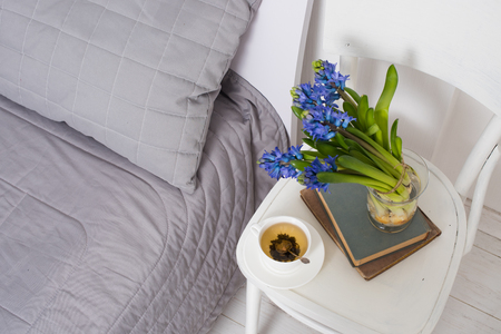 Clean white bedroom interior closeup, cup of tea and hyacinth flowers on a chair. Home interior decor.の写真素材