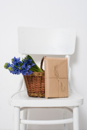 Spring flowers and wrapped gift, blue hyacinth in a basket on a vintage chair in white room interior.の写真素材