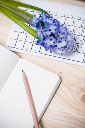Working table with paper notebook, computer keyboard and flowers. Lovely office closeup top view.の写真素材