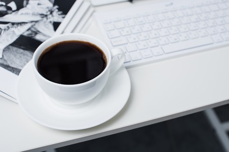 Modern office interior closeup, cup of coffee and computer keyboard. Business objects on white working table background.の写真素材