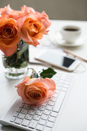 Bright white office table decor with fresh flowers, computer keyboard and smart phone. Woman's modern workspace, interior details.の写真素材