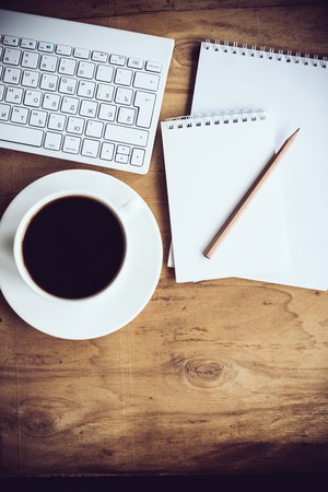 Vintage hipster style office table decor with cup of coffee, computer keyboard and smart phone. Blogger's modern workspace, interior details, top view.の写真素材