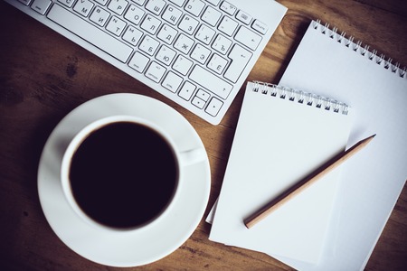 Vintage hipster style office table decor with cup of coffee, computer keyboard and smart phone. Blogger's modern workspace, interior details, top view.の写真素材