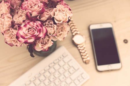 Woman blogger's office table closeup, flowers with keyboard and smart phone on a wooden background, top view.の写真素材