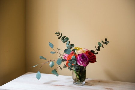 Bouquet of colorful roses in a vase on the table, by tha wall space background. Summer home interior decor.の写真素材