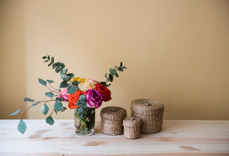 Bouquet of colorful roses in a vase  and decorative boxes on the table, by tha wall space background. Summer home interior decor.の写真素材