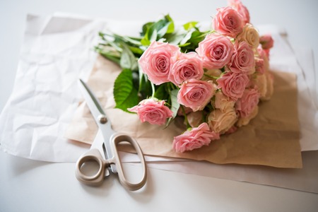 Florist's workspace: bouquet of fresh roses and scissors on an old vintage wooden board table.の写真素材