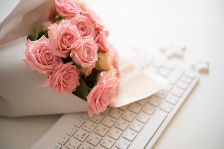 Bouquet of pink and beige roses on white computer keyboard, modern workplace closeupの写真素材